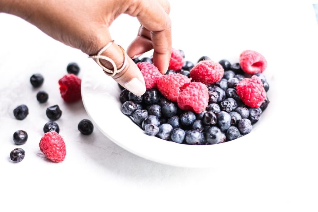 Close-up of hand picking fresh raspberries and blueberries from a white bowl.